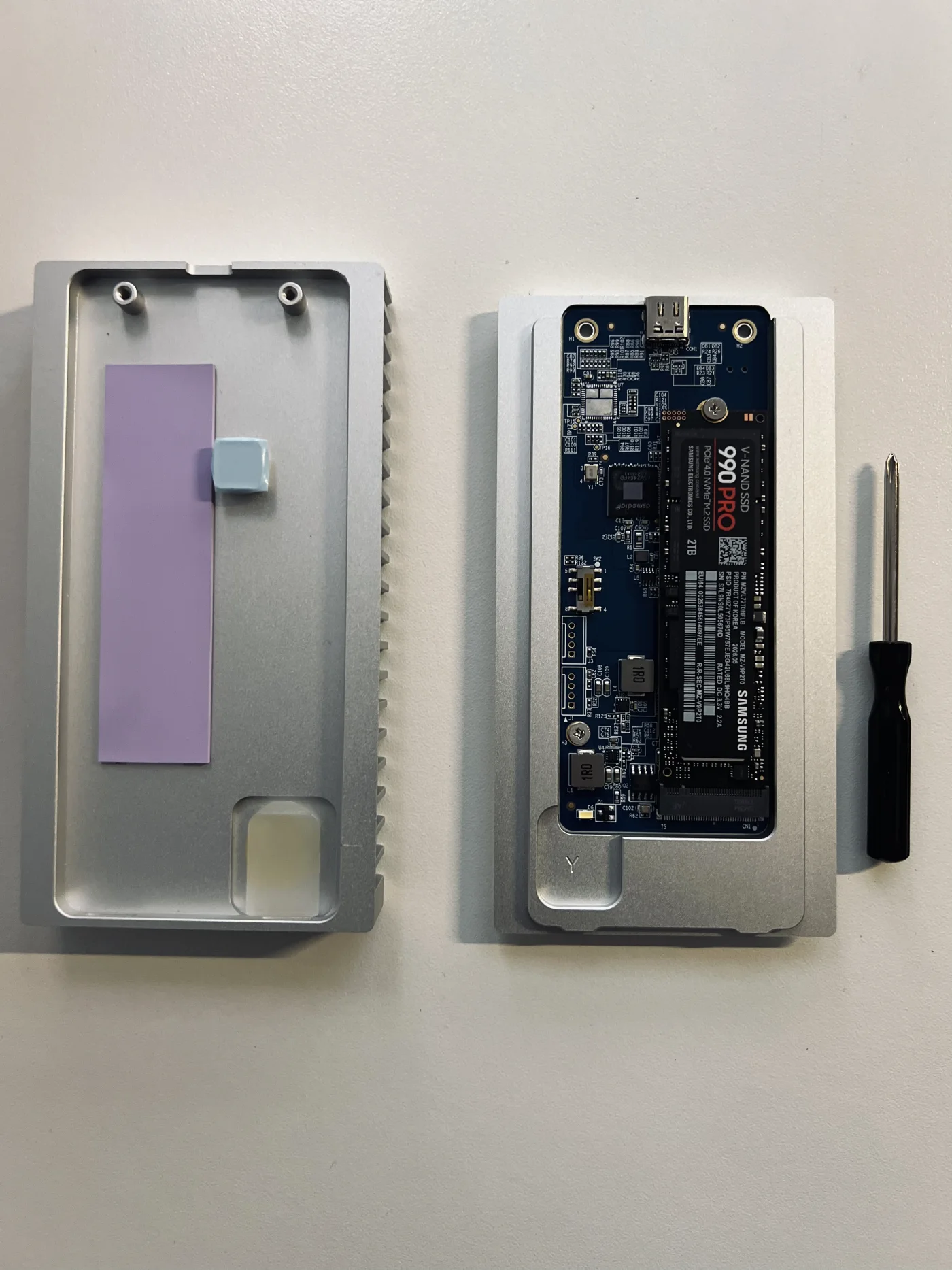 Samsung 990 PRO installed inside the OWC Express 1M2 enclosure, with the enclosure cover and screwdriver beside it.